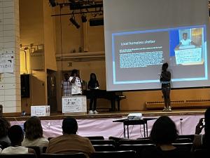 Johnson Middle School students presenting on stage about their supply drive for a Homeless Shelter