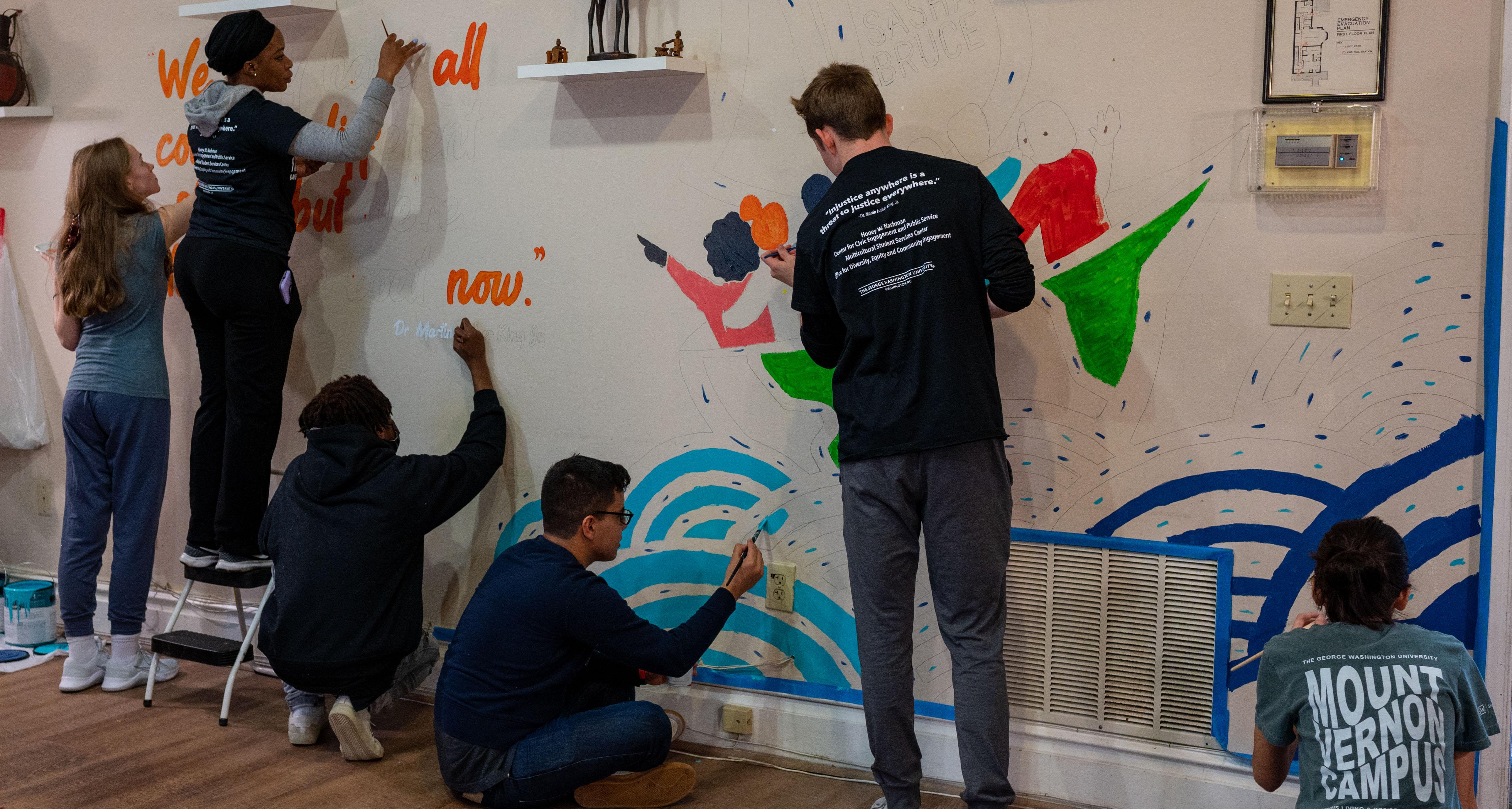 Students assisting with painting a mural on a wall at a youth shelter on MLK Day of Service and Leadership